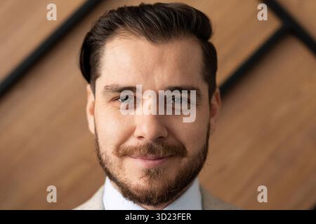 Ritratto ravvicinato di un uomo d'affari con la barba sullo sfondo di una parete d'ufficio in legno Foto Stock