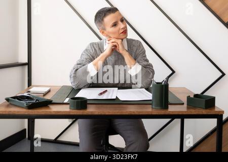 Donna avvocato sul posto di lavoro a un tavolo con documenti si siede a pensare Foto Stock