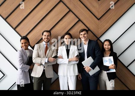 I giovani dipendenti dell'azienda con un sorriso in faccia si trovano in ufficio appoggiati al muro guardando la telecamera Foto Stock