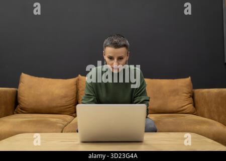 Donna al lavoro su computer portatile mentre è seduto sul divano Foto Stock