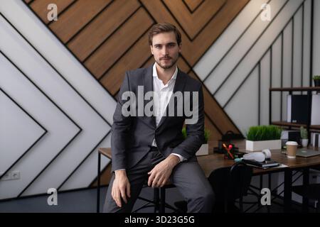 Un avvocato maschile siede in ufficio sul tavolo e guarda la telecamera Foto Stock