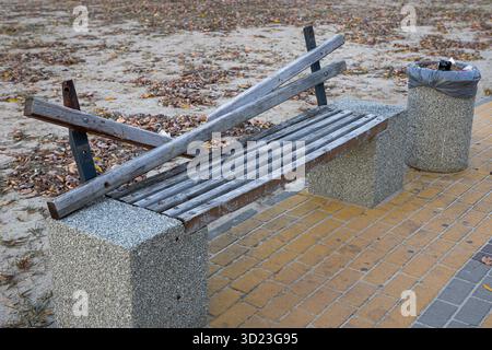 Una panchina di legno rotta si trova su un percorso in mattoni. Foto Stock