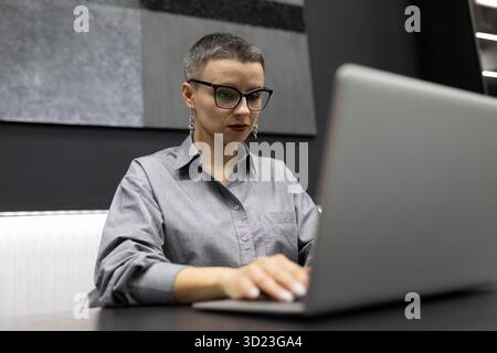 Programmatore donna maschile con taglio corto che lavora su un notebook in un ufficio robusto Foto Stock