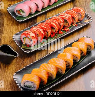 Piatti di sushi con rotoli assortiti esposti su un tavolo di legno Foto Stock