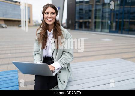 Giovane donna in cuffia con laptop sullo sfondo di un edificio moderno Foto Stock