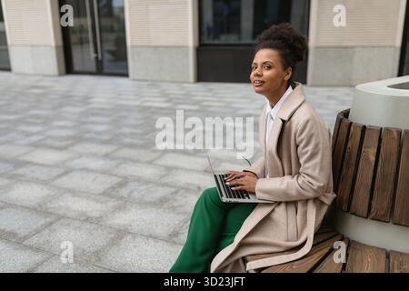 Ritratto di una giovane donna nera di successo con un portatile su una panchina vicino al business center Foto Stock