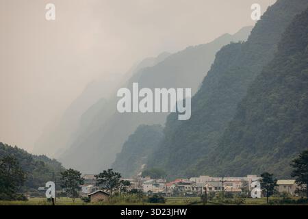Le montagne nebbiose si stagliano su un piccolo villaggio immerso in una lussureggiante valle verde. TR˘ng KH·nh District, Cao Bang, Vietnam Foto Stock