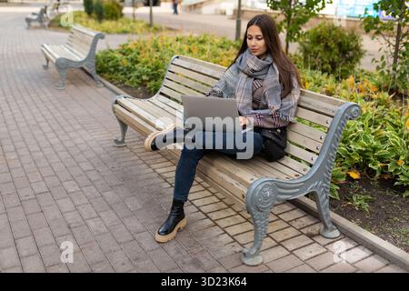 Giovane donna che lavora su un notebook online nel parco con abiti caldi Foto Stock