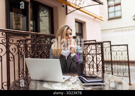 Imprenditrice donna che lavora su un laptop online dal caffè cittadino per strada Foto Stock
