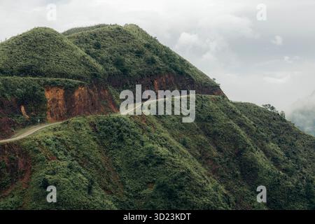 Una strada tortuosa serpeggia attraverso lussureggianti colline verdi sotto un cielo nuvoloso. Distretto di Binh Lieu, Quang Ninh, Vietnam Foto Stock