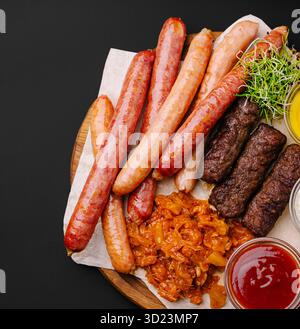 Salsicce e carni alla griglia servite con i contorni su una tavola di legno Foto Stock
