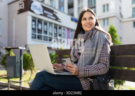 Ritratto di una giovane donna d'affari di successo che lavora online su un notebook con una tazza di caffè e guarda a distanza con Foto Stock