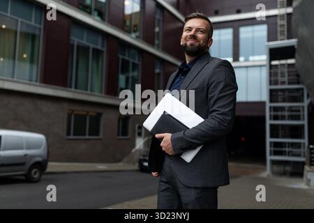 Ritratto di un uomo d'affari adulto di successo con un portatile in mano sullo sfondo dell'ingresso dell'ufficio Foto Stock