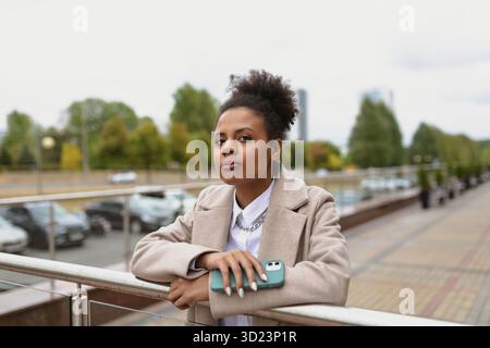 Ritratto di una donna afroamericana seria con un cellulare sullo sfondo della città Foto Stock