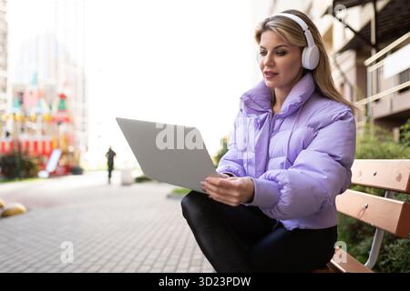 Donna matura con le cuffie che lavora su un notebook all'aperto Foto Stock
