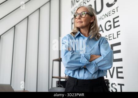 La donna anziana di medio-età di affari osserva intently al lato bene nell'ufficio, concetto di sviluppo riuscito di affari Foto Stock