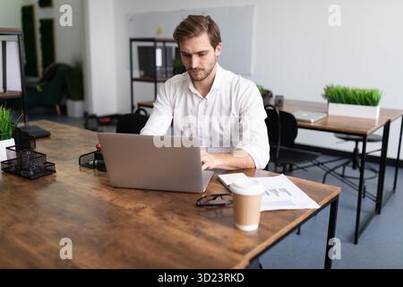 Un giovane uomo d'affari con una camicia bianca lavora sui computer portatili in ufficio Foto Stock