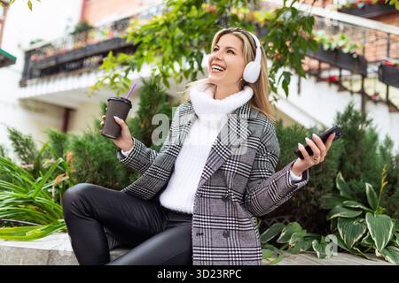 Una donna adulta ama ascoltare musica con le cuffie sullo sfondo di un parco cittadino Foto Stock