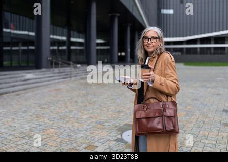 Donna di successo dai capelli grigi adulta donna d'affari sullo sfondo di un edificio per uffici Foto Stock