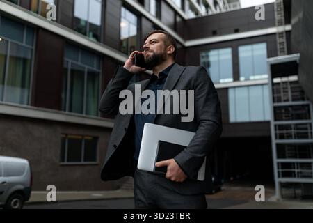 Ritratto di un uomo d'affari con un computer portatile che parla al telefono con abiti da lavoro sullo sfondo di un business center, Co Foto Stock