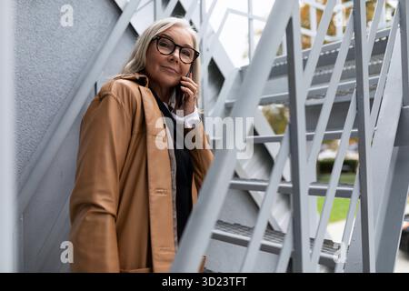 Donna d'affari matura che parla al telefono sulle scale fuori Foto Stock