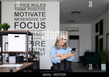 Donna d'affari autosufficiente e sicura di sé che tiene in mano un telefono in ufficio Foto Stock