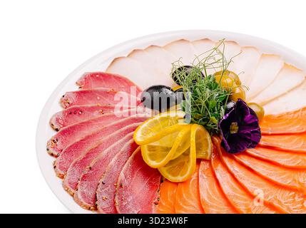 Un piatto ben organizzato con salmone a fette sottili, tonno in crosta di pepe e fette di carne bianca, guarnite con limone Foto Stock