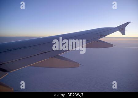 Ala dell'aereo vista da un posto vicino al finestrino che vola sopra le nuvole durante l'alba. Foto Stock