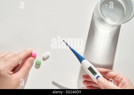 Pillole per mani e termometro digitale su superficie bianca con vetro Foto Stock