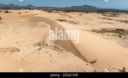 Veduta aerea delle dune di sabbia di Phan Rang, Vietnam: Ampio paesaggio desertico con dune scolpite e montagne lontane sotto il cielo blu. Foto Stock