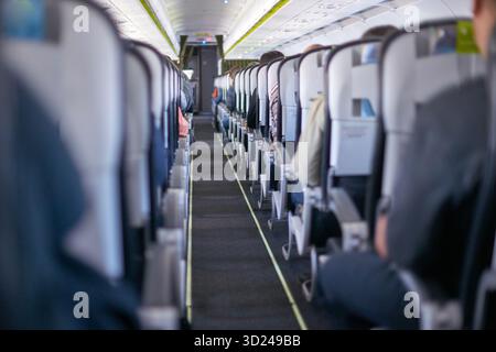 Vista interna della cabina dell'aereo commerciale con passeggeri seduti e corsia Foto Stock