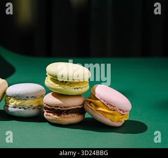Selezione di macaron colorati su una superficie verde con sfondo vivace Foto Stock
