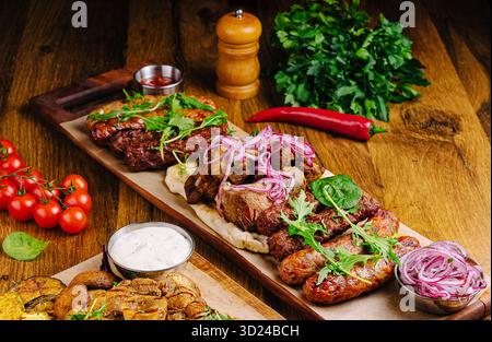 Carni alla griglia servite su un piatto di legno con decorazioni e contorni Foto Stock