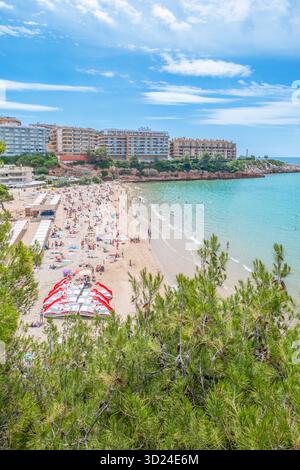 Spiaggia affollata e acque turchesi del Mar Mediterraneo in una giornata di sole a Salou, Costa Daurada, Spagna. Gli alti resort hotel costeggiano la costa rocciosa Foto Stock