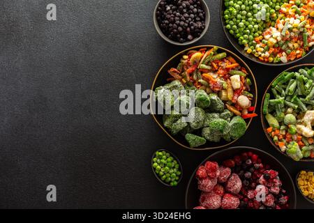 Una varietà di verdure e frutta congelate disposte in piatti, su sfondo scuro, catturando l'essenza della conservazione estiva per l'inverno Foto Stock
