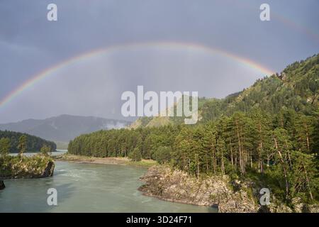 Maestoso doppio arcobaleno sulle montagne boscose e sul fiume sotto il cielo nuvoloso Foto Stock