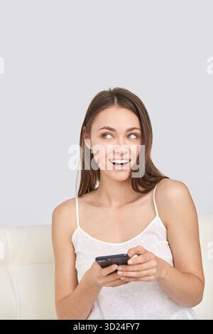 Giovane donna caucasica che sorride e tiene in mano lo smartphone nella parte superiore bianca Foto Stock