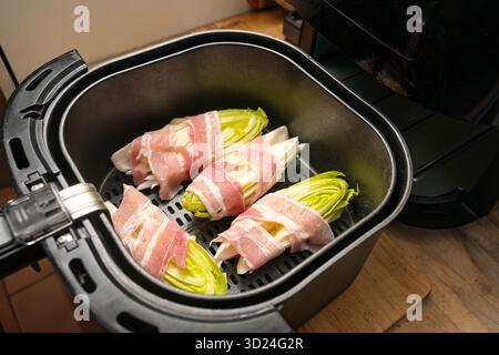 Cicoria tagliata a metà avvolta in strisce di pancetta nel cestello di una friggitrice ad aria calda, cottura rapida e semplice, messa a fuoco selezionata, profondità di campo ristretta Foto Stock