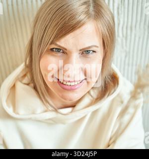 Donna matura caucasica sorridente con capelli biondi con cappuccio bianco seduta Foto Stock