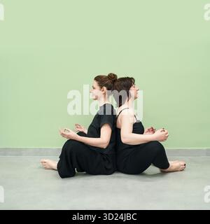Due donne caucasiche adulte che meditano in posa yoga sul pavimento grigio Foto Stock