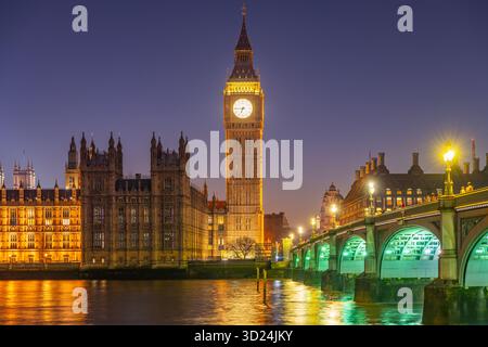 Splendida vista del Big Ben e delle camere del Parlamento immerse nelle luci dorate di notte. Il Westminster Bridge è illuminato, riflettendo la vibrante atmosfera di Londra. Foto Stock