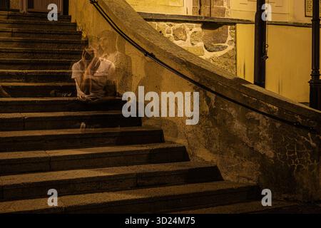Personaggio spettrale a lunga esposizione seduto su antiche scale di pietra di notte in una città storica. Foto Stock