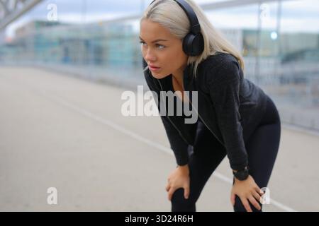 Donna concentrata nell'abbigliamento sportivo che ascolta la musica durante le pause fitness urbane Foto Stock