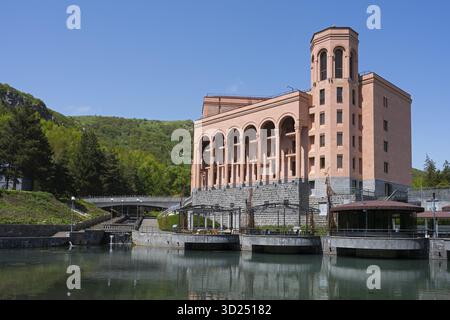 Grande edificio rosa con colonne su un fiume con un ponte circondato da verdi colline e cielo limpido, l'Hotel Grand Resort Jermuk, Jermuk, centro benessere, V Foto Stock