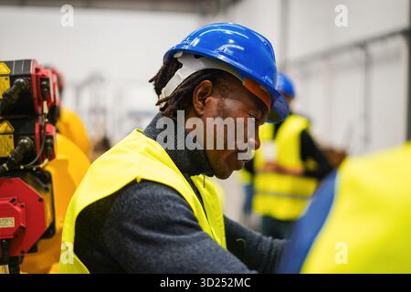 Uomo afroamericano che lavora all'interno di una fabbrica di ingegneria meccanica - tecnologia, apprendimento automatico, intelligenza artificiale e concetto industriale - Focus sul volto maschile Foto Stock