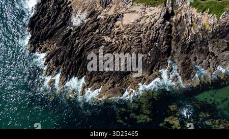 Vista aerea delle onde del mare che si infrangono contro una costa rocciosa in una mattinata luminosa Foto Stock