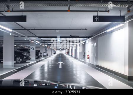 Svuota la lunga corsia in un moderno garage sotterraneo con auto parcheggiate generiche. Visione grandangolare, immagine blu, nessuna persona Foto Stock