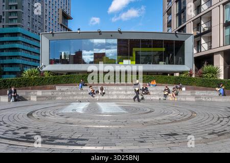 Veduta di Merchant Square, Paddington Basin, Londra W2, Inghilterra, Regno Unito, spazio pubblico con persone sedute su gradini in una giornata di sole d'autunno Foto Stock