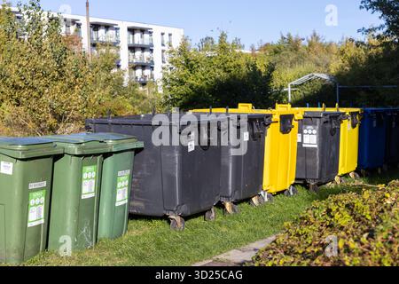 Poznan, Polonia - 24 settembre 2025: Grandi bidoni di diversi colori delimitano l'erba verde vicino agli appartamenti, mostrando la raccolta organizzata dei rifiuti urbani e l'eco-f Foto Stock