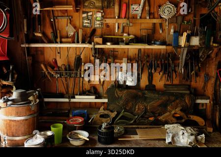 Parete in legno dell'officina che mostra una varietà di utensili manuali tra cui martelli, seghe, cacciaviti, pinze e strumenti di misurazione disposti su scaffali e scaffali Foto Stock